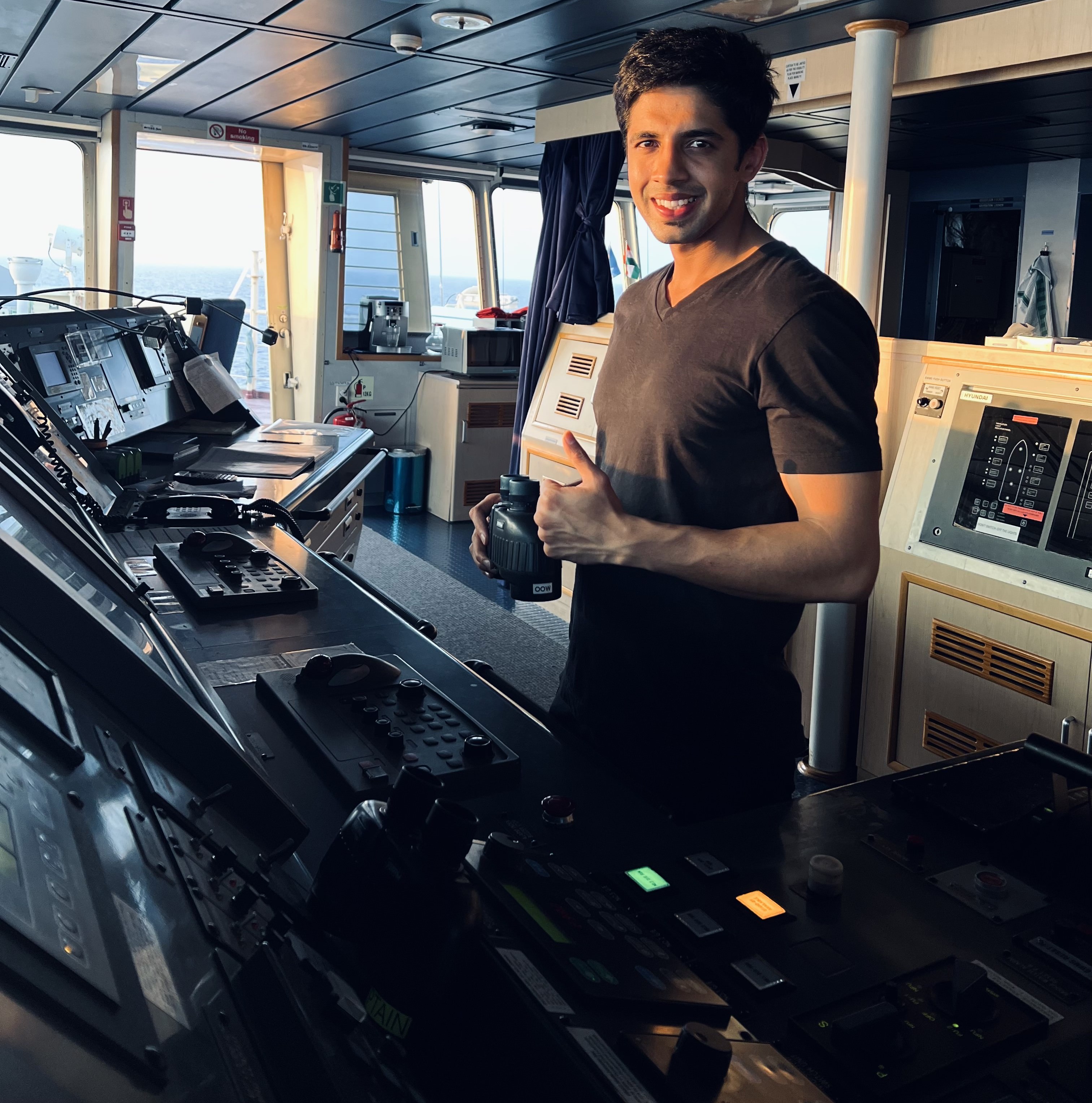 Karanvir standing on the bridge of a ship keeping watch with thumbs up looking at the camera